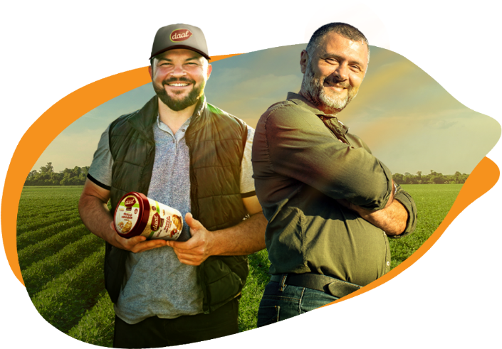 Dois homens sorrindo, um deles segurando um pote de amendoim, com um campo ao fundo.