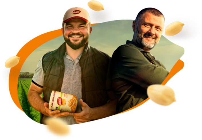Dois homens sorrindo, um deles segurando um pote de amendoim, com um campo ao fundo.